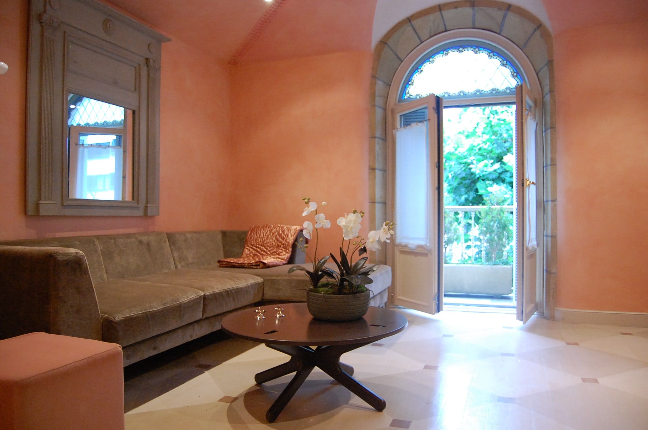 Salón con paredes de estuco rosado, sofá de terciopelo y puerta arqueada de madera