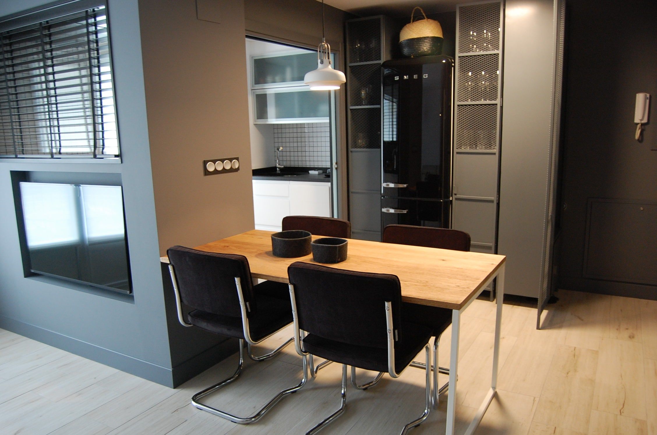 Comedor con mesa de madera y sillas negras abierto a la cocina, de estilo industrial