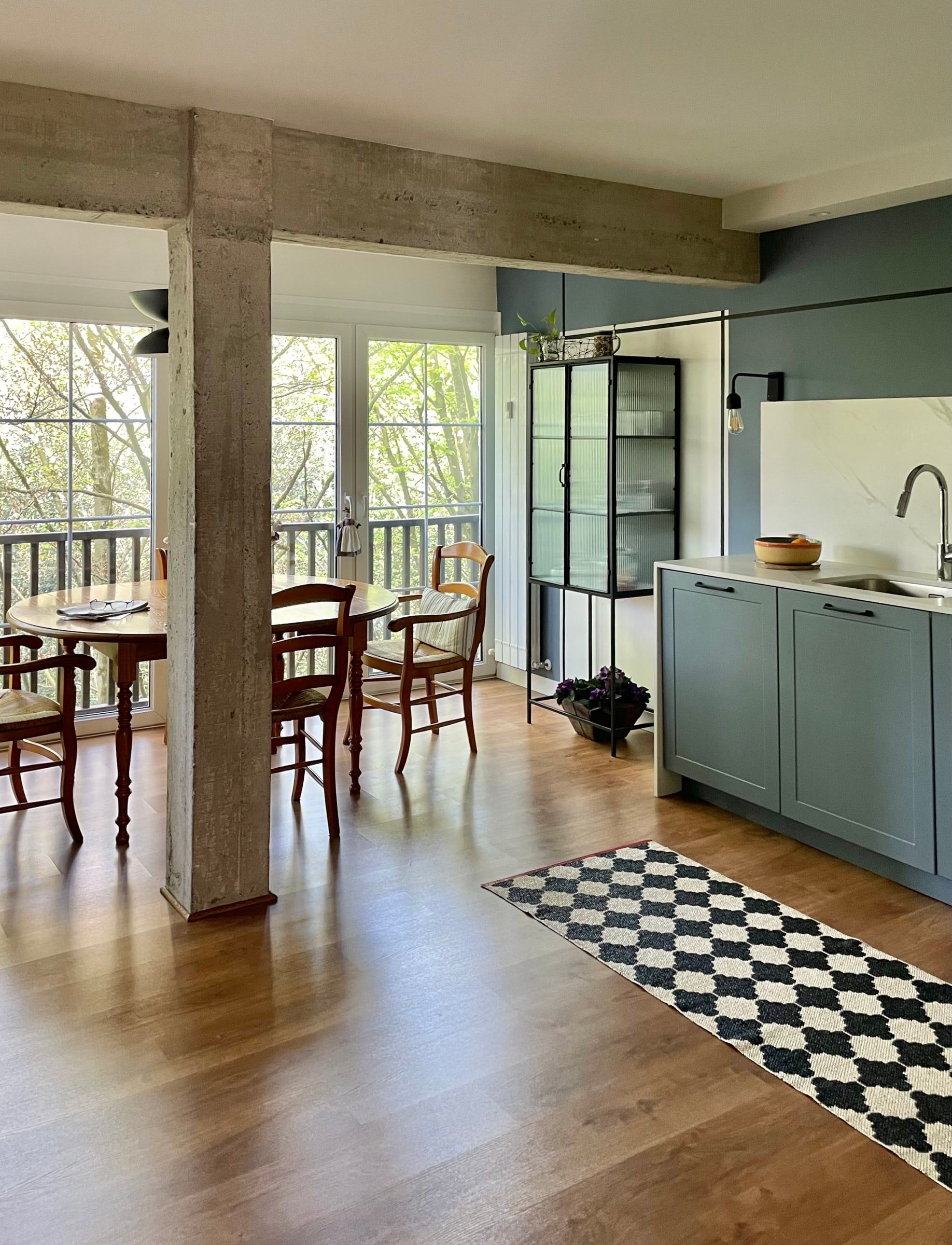 Después: Cocina abierta al comedor con muebles azul grisáceo, viga de madera y alfombra de damero