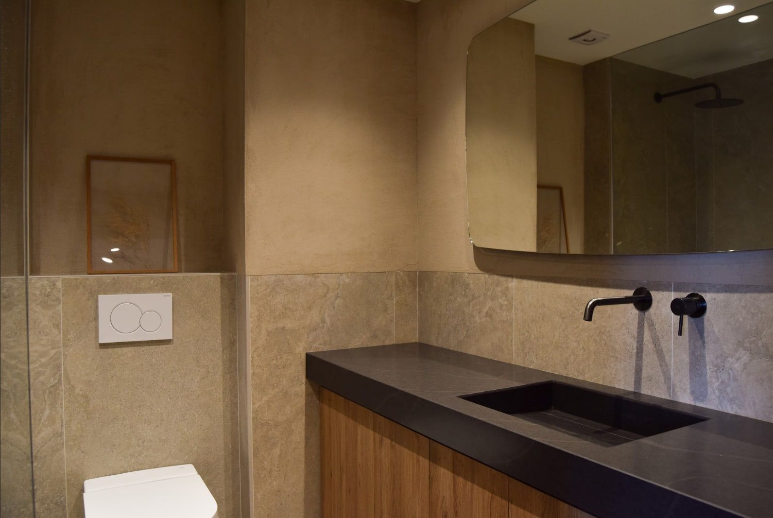 Lavabo con encimera negra y mueble de madera en baño de piedra