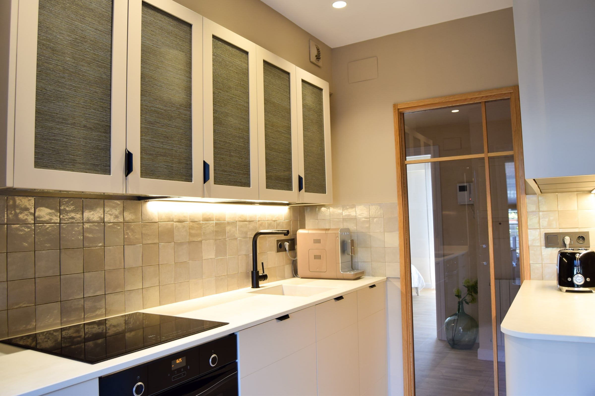 Cocina con muebles altos de puertas texturizadas y puerta de cristal al fondo