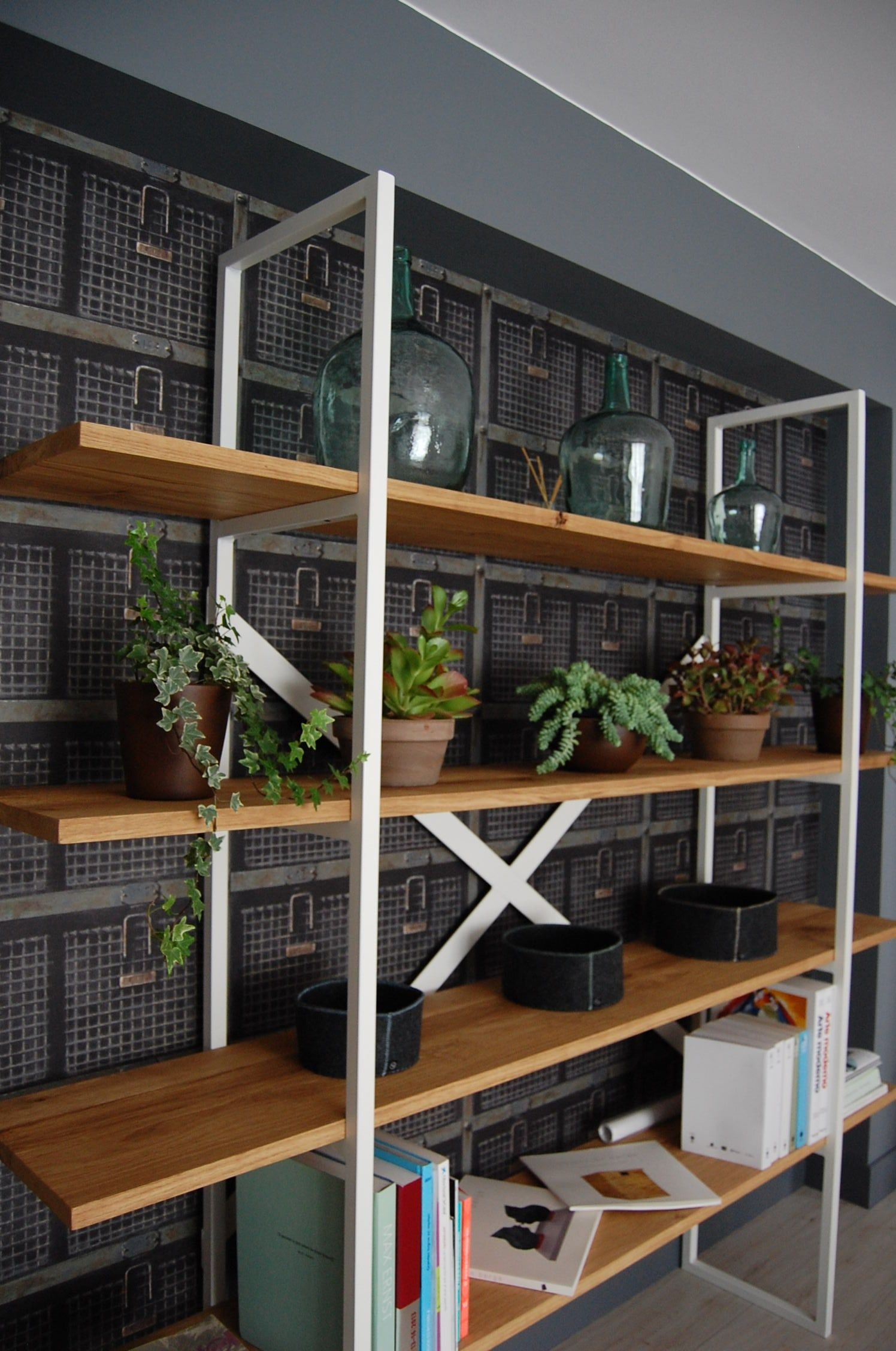 Estantería de metal blanco y madera con plantas sobre pared de rejilla negra