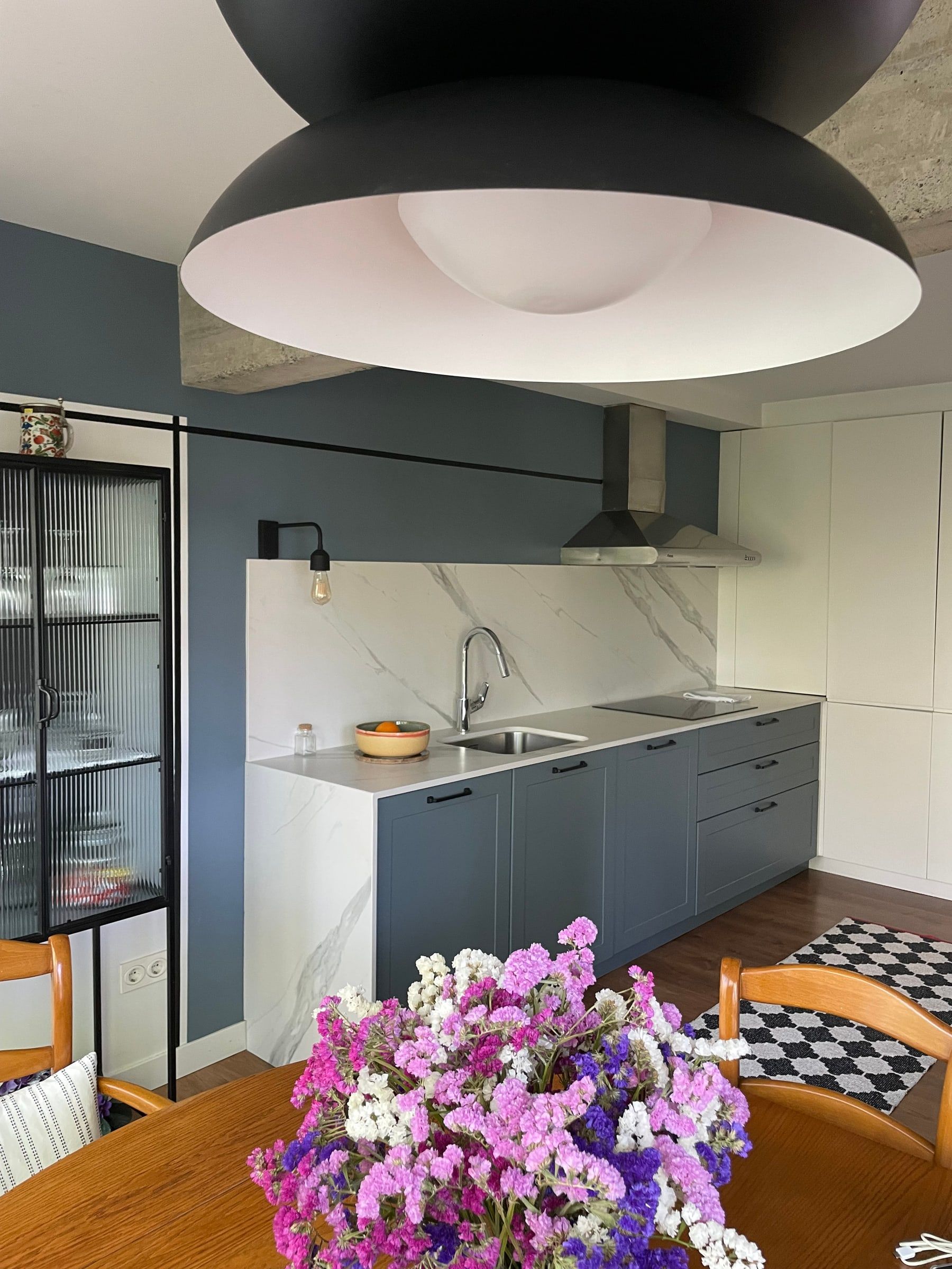 Cocina en azul grisáceo vista desde la mesa del comedor con flores
