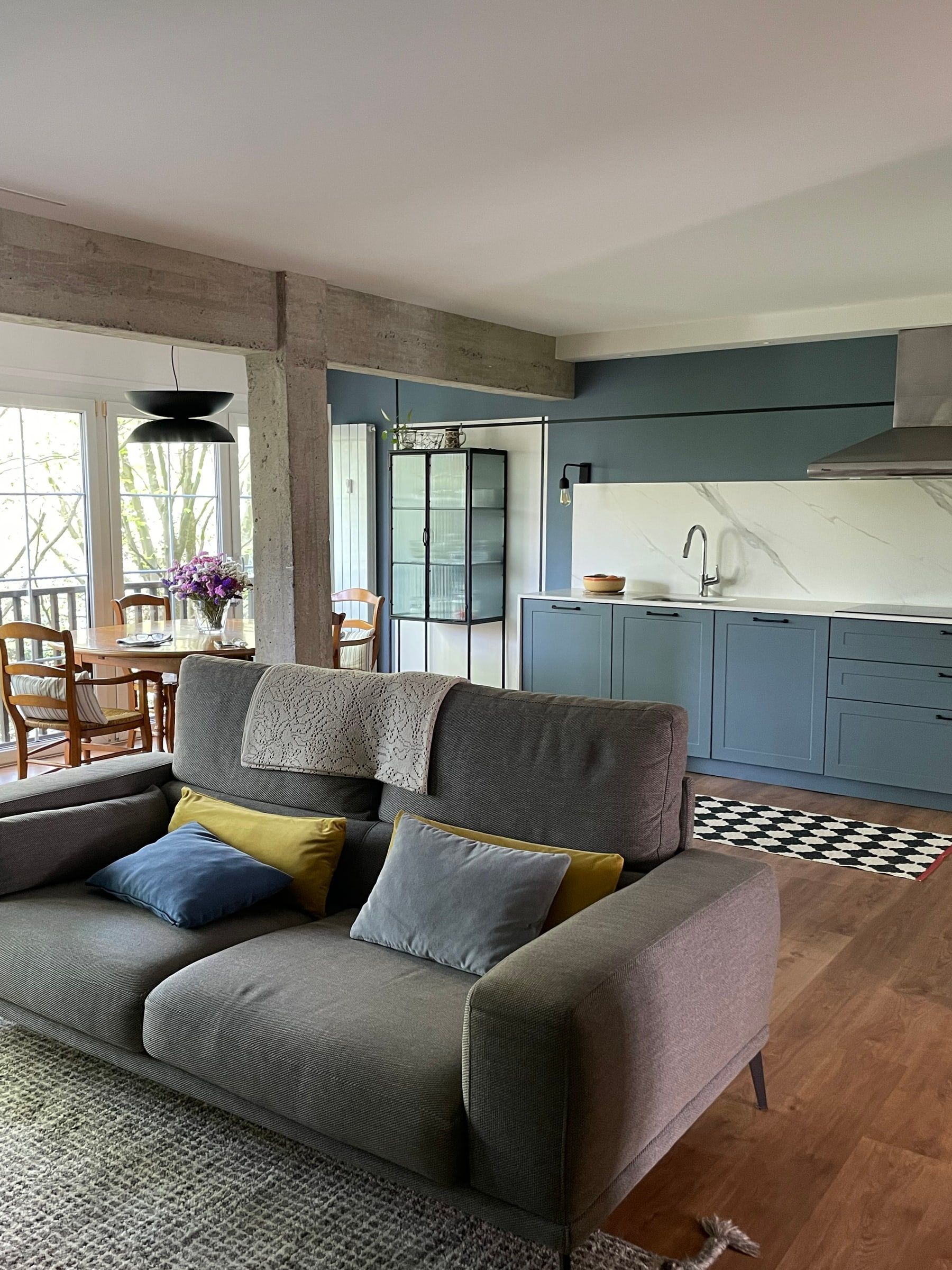 Salón con sofá gris abierto a la cocina azul y la vitrina de cristal